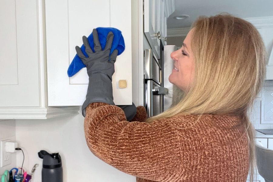 Woman cleaning white kitchen cabinet