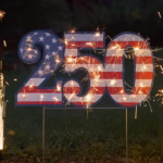 A patriotic 250 lawn sign with sparklers around it.