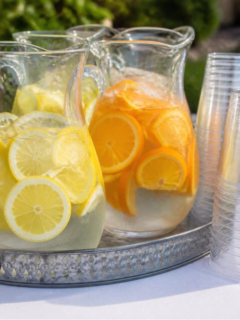 refreshing water with lemons and oranges in it and cups on the side
