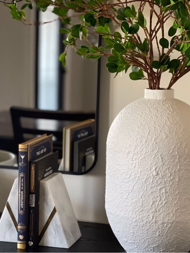 a white vase with green twigs coming out of it and two books in between bookends