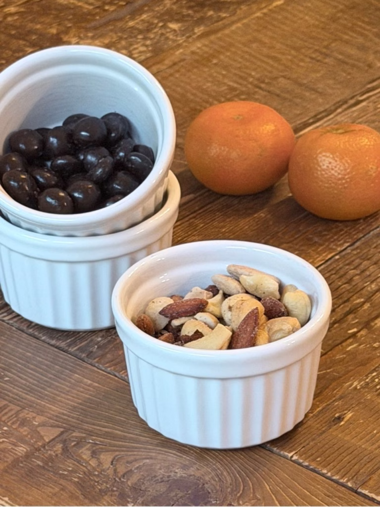ramekins filled with nuts and chocolate covered acai with two clementines behind the bowls