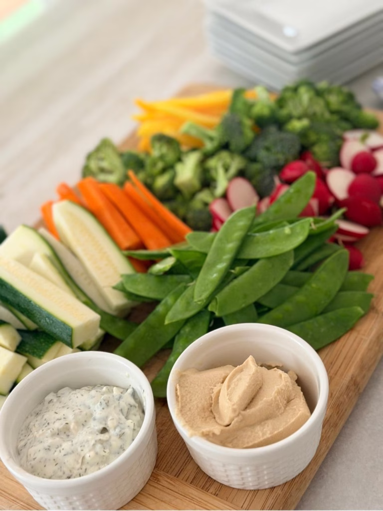 two ramekins with dips in them and veggies on a wooden board