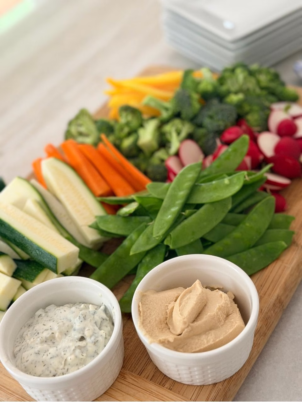 two ramekins with dips in them and veggies on a wooden board
