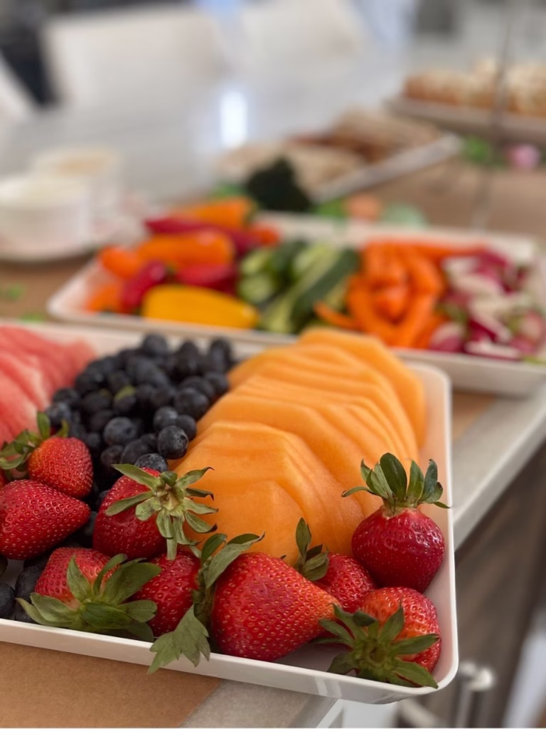 Two white platters with on focusing on fruit like cantelope, strawberries and blueberries